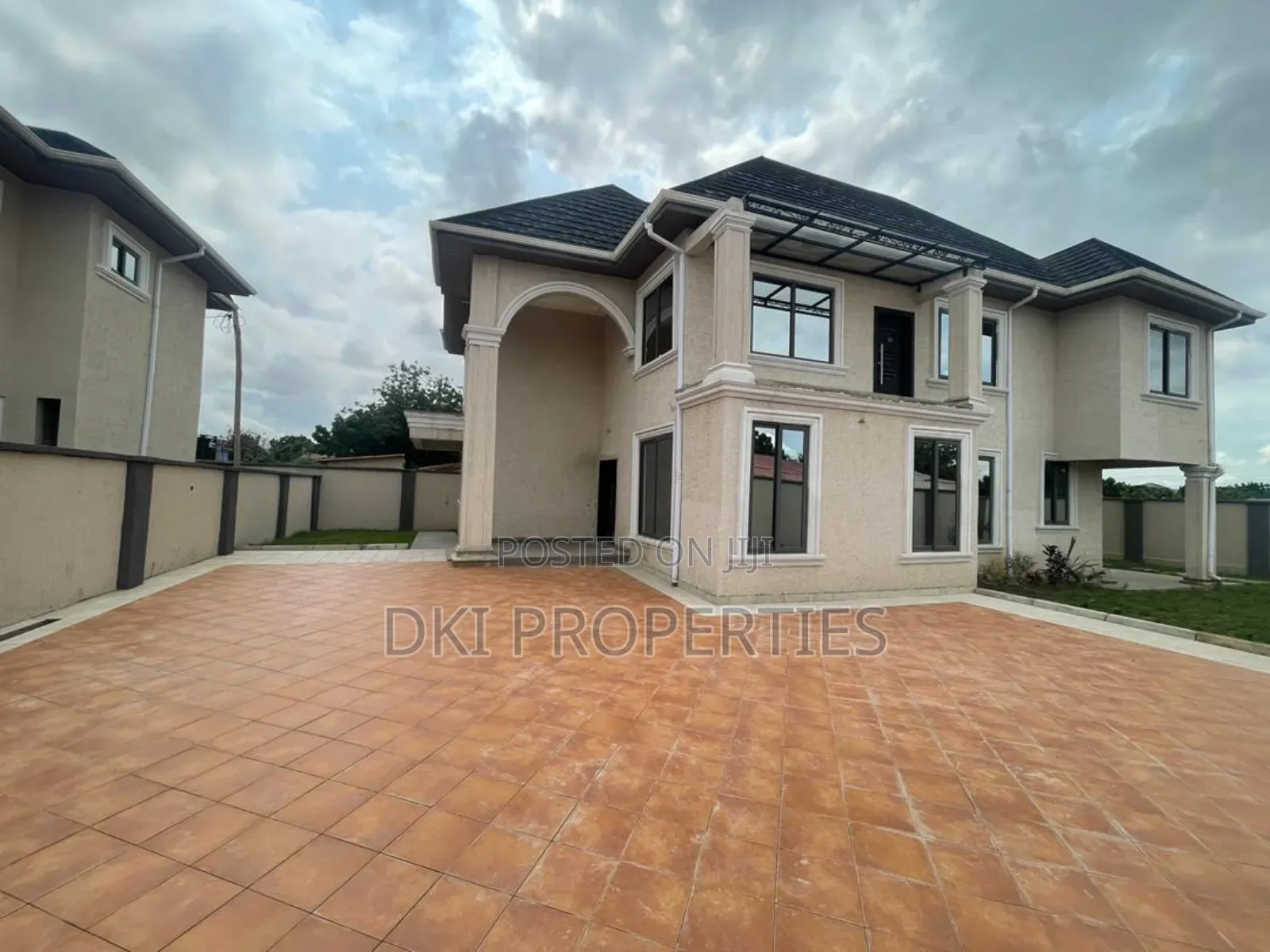 Exterior view of a newly-built, semi-furnished 4-bedroom executive townhouse in Adenta/Amanfrom, highlighting the large tiled compound, automated gate, and space for multiple cars.