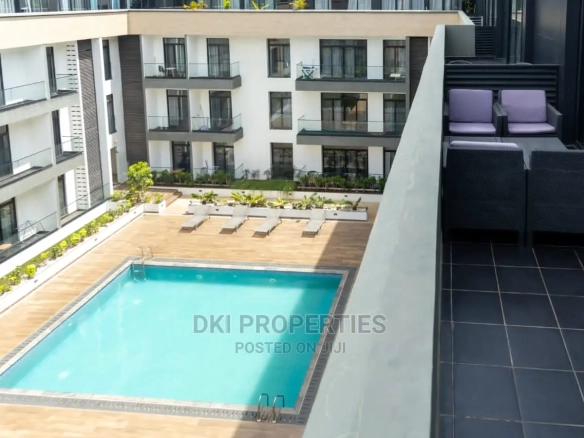 Interior view of a fully-furnished 2-bedroom luxury apartment in Embassy Gardens, Cantonments, showing the modern kitchen and living area with a balcony view.