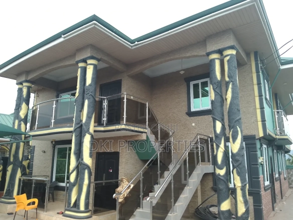 Exterior view of a newly-built, two-storey 6-bedroom detached house in the Oyibi Valley View Area, showcasing the security fencing, gated entrance, and ample parking space.