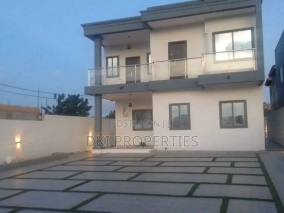 Exterior view of a newly-built, semi-furnished 4-bedroom self-compound house in Adenta New Legon, showing a spacious paved compound with carpet grass and parking for multiple cars.